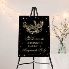 a welcome sign for a masquerade party on an easel with lights in the background