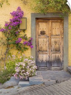 an old wooden door in front of a yellow building with purple flowers