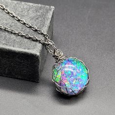 Embrace the mystery of the universe with this round galaxy cabochon set in braided darkened steel! It is totally handmade, with unique original design. The double sided pendant features amazing iridescent sparkling colors that opalesce and bot refracts and light to show a rainbow nebula on one side and a black backed cabochon.  It is made with heat darkened steel, using man-made cabochons instead of mined gems, so it is very environmentally friendly. Iridescent Opal Round Jewelry, Iridescent Round Opal Jewelry, Iridescent Opal Jewelry, Handmade Iridescent Metal Jewelry, Mystical Metal Round Pendant Jewelry, Mystical Round Pendant Metal Jewelry, Unique Iridescent Round Jewelry, Unique Iridescent Opal Jewelry, Iridescent Metal Jewelry For Jewelry Making