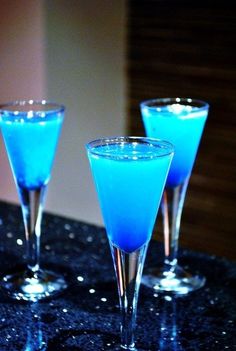 three martini glasses sitting on top of a table next to each other, with blue liquid in them