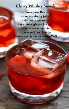 two glasses filled with red liquid and ice on top of a wooden table next to cherries