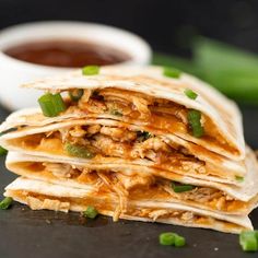 a stack of chicken quesadillas with green onions and jalapenos