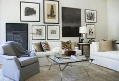 a living room filled with white furniture and pictures on the wall above it's coffee table