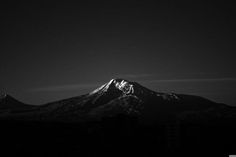 a black and white photo of the top of a mountain in the night sky with clouds