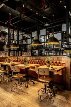 an empty restaurant with wooden tables and leather chairs, hanging lights and potted plants