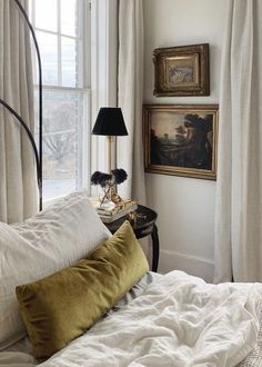 a bed with white sheets and pillows in front of a painting on the wall next to a window