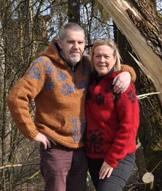 an older man and woman standing next to each other in the woods with their arms around each other