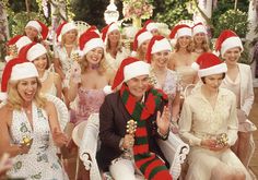 a group of women wearing christmas hats and sitting on white chairs in front of trees