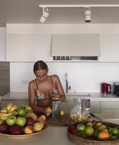 a woman standing in a kitchen next to a bowl of fruit