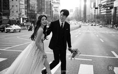 a man and woman walking across a street holding hands in the middle of an intersection