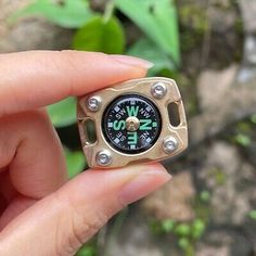 a person holding a small compass in their left hand and green plants in the background