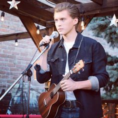 a young man holding a guitar while standing in front of a microphone