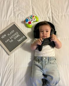 a young child laying on top of a bed holding a game controller next to a sign that says new player has entered the game