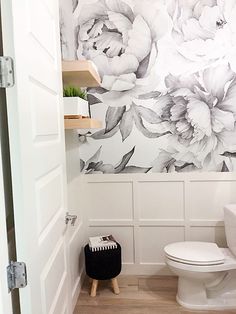 a white toilet sitting next to a wall with flowers on it