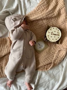 a baby laying on top of a bed next to a box with a cake in it