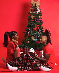 two people sitting in front of a christmas tree