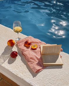 an open book sitting on top of a table next to a glass of wine and fruit