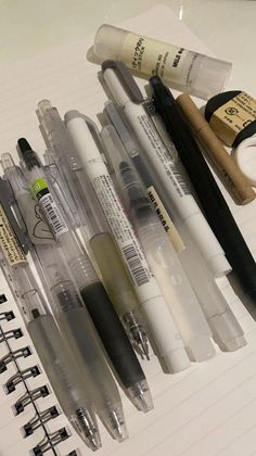 several pens and markers are lined up on a notebook