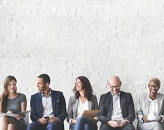 group of people sitting in front of a white brick wall talking and smiling at each other