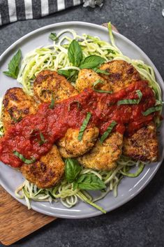 chicken parmesan with spaghetti and tomato sauce on a white plate next to a wooden cutting board