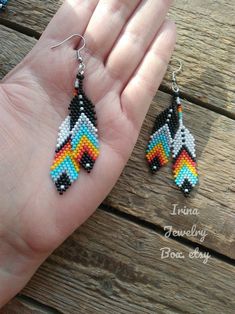 a hand holding two pairs of colorful beaded earrings