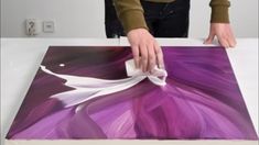 a person is painting on a table with purple and white paint, while another person holds a piece of paper in their hand