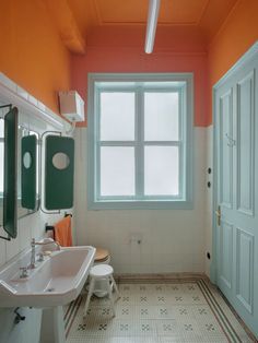 an orange and white bathroom with two sinks, mirror, and toilet paper dispenser