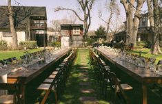 a long table is set up in the yard for an outdoor dinner party with clear glasses and place settings