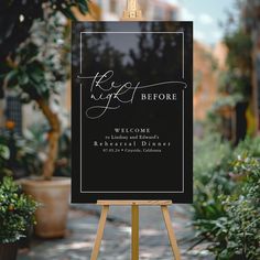 a black and white sign sitting on top of a wooden easel next to potted plants