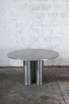 two stainless steel tables sitting in front of a white brick wall and concrete flooring