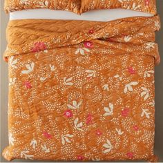 an orange comforter set with white and pink flowers on the bottom, along with two pillows