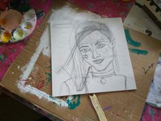 a drawing of a woman's face sitting on top of a cardboard box next to paintbrushes