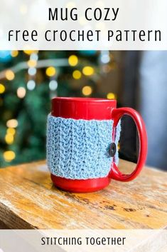 a red coffee cup sitting on top of a wooden table next to a christmas tree