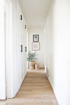 an empty hallway with white walls and wooden flooring, framed pictures on the wall