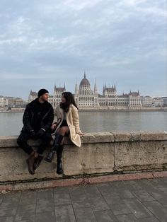 a man and woman sitting on a wall next to the water