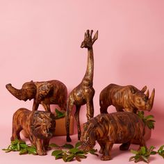 three wooden animals and one giraffe are standing next to each other on a pink background