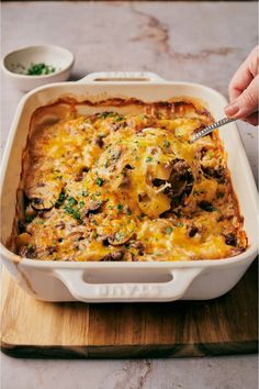 a casserole dish with mushrooms and cheese being spooned into the casserole