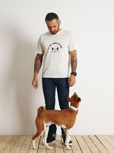 a man standing next to a brown and white dog on a wooden floor in front of a wall