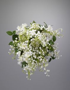 a bouquet of white flowers with green leaves on a gray background in front of a grey wall