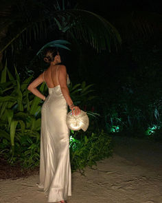 a woman in a white dress is holding a straw hat and looking at the ground