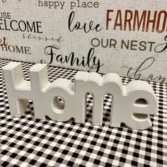 the word home is made out of white letters on a checkered tablecloth with a black and white wall behind it