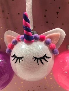 an ornament shaped like a unicorn's head with pink and purple pom poms