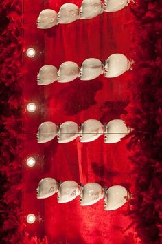 several white masks are lined up against a red wall with lights on them and in the middle