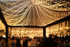 the inside of a tent is lit up with string lights and white tablecloths