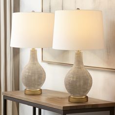 two lamps sitting on top of a table next to a book and flower vase in front of a window