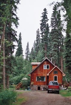 a red truck parked in front of a wooden cabin surrounded by tall trees and evergreens