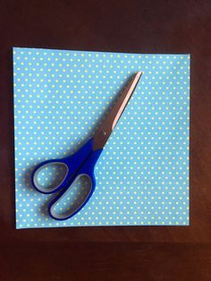 a pair of blue scissors sitting on top of a piece of paper with white dots