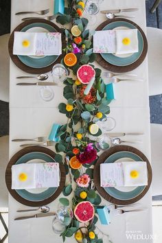 the table is set with plates, silverware and grapefruits on it