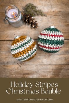 two crocheted christmas ornaments sitting on top of a wooden table next to a candle