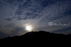 the sun is shining through some clouds in the sky over a mountain range at night